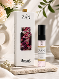 A boxed fragrance product labeled ZĀN Smart Khareedat stands beside a small clear spray bottle with a black cap on a stone slab. The box is white with a floral window and the same ZĀN branding, set in a styled interior with soft flowers and greenery.