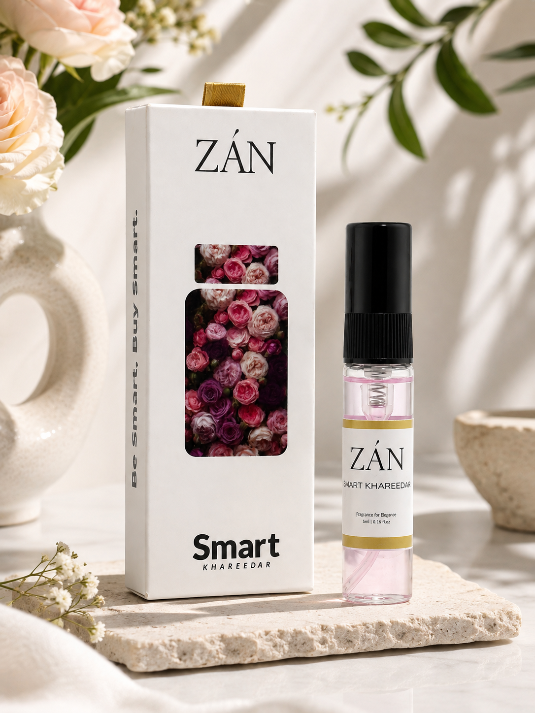 A boxed fragrance product labeled ZĀN Smart Khareedat stands beside a small clear spray bottle with a black cap on a stone slab. The box is white with a floral window and the same ZĀN branding, set in a styled interior with soft flowers and greenery.